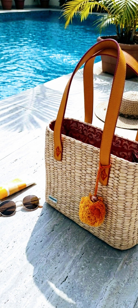 Hand Woven KAUNA GRASS bag with pom-pom detail by a poolside