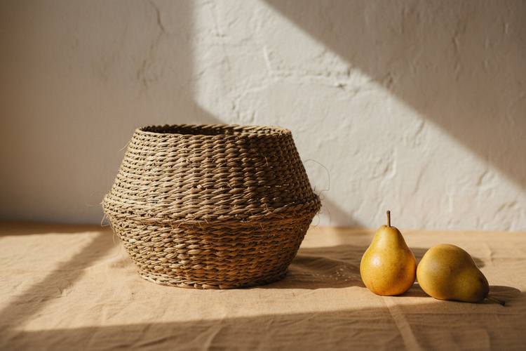 "Handwoven sabai grass basket on a linen surface with golden pears — natural fibre home decor by Grasscrafts"