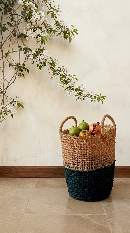 Hand Woven sabai grass basket with colorful design on a tiled floor with a light-colored wall and floral branch in the background.