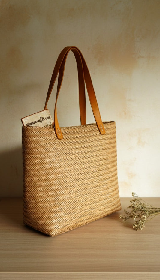 Woven straw tote bag with leather handles on a wooden surface. This is a sitalpati bag.