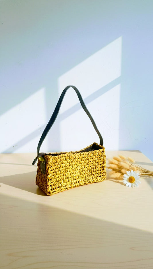 Woven handbag on a wooden surface with a light blue gradient background. Indian artisan handmade crossbody bag, sustainable fashion.