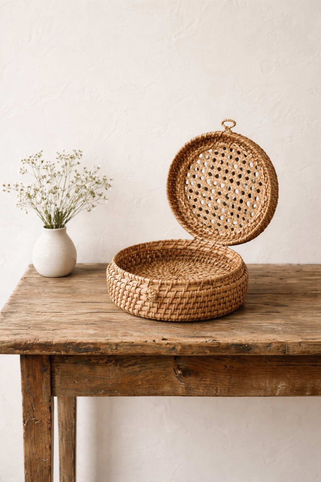 hand Woven basket with a lid on a wooden table next to a small white vase with flowers.
